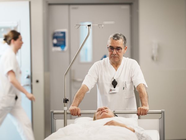 Patienttransport i sjukhuskorridor med patient på säng och transportpersonal.